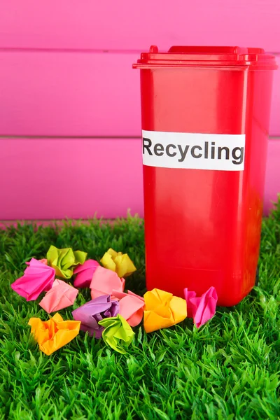 Recycling-Tonne mit Papieren auf Gras auf rosa Hintergrund — Stockfoto