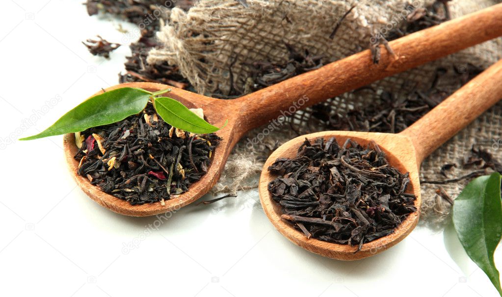 Dry tea with green leaves in wooden spoons, isolated on white