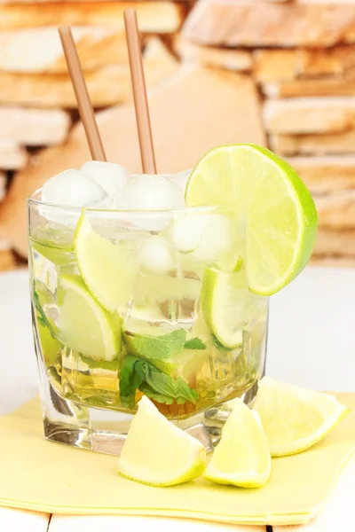 Glass of cocktail with lime and mint on white wooden table on stone wall background — Stock Photo, Image