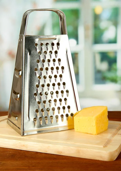 Ralador de metal e queijo na placa de corte, sobre fundo brilhante — Fotografia de Stock
