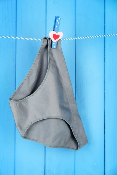 Womans panties hanging on a clothesline, on blue wooden background — Stock Photo, Image