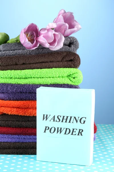 Pile of colorful towels, wash powder, on blue background — Stock Photo, Image