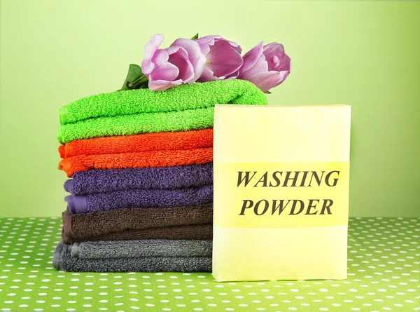 Pile of colorful towels, wash powder, on green background — Stock Photo, Image