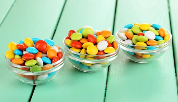Färgglada karameller i glas skålar på grön trä bakgrund — Stockfoto