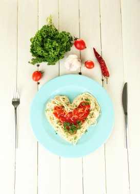 Cooked spaghetti carefully arranged in heart shape and topped with tomato sauce, on wooden background