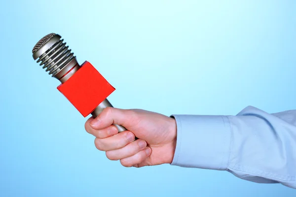 Male hand with microphone on blue background — Stock Photo, Image