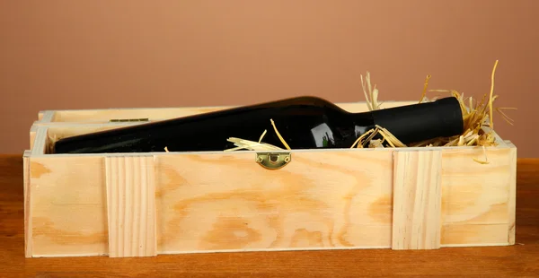 Wine bottle in wooden box on wooden table on brown background — Stock Photo, Image