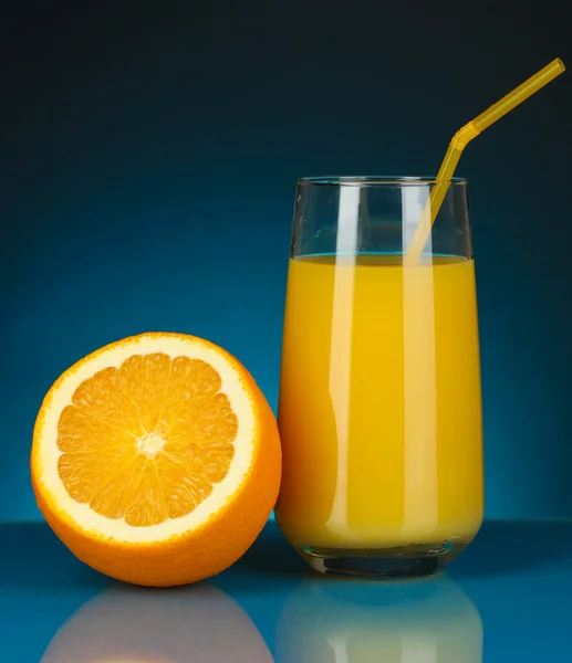 Sumo de laranja delicioso em vidro e laranja ao lado dele no fundo azul escuro — Fotografia de Stock