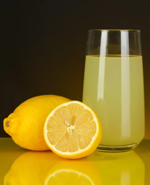 Delicioso zumo de limón en vaso y limones al lado sobre fondo naranja oscuro — Foto de Stock