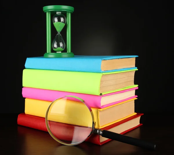 Color books with magnifying glass on table on black background — Stock Photo, Image