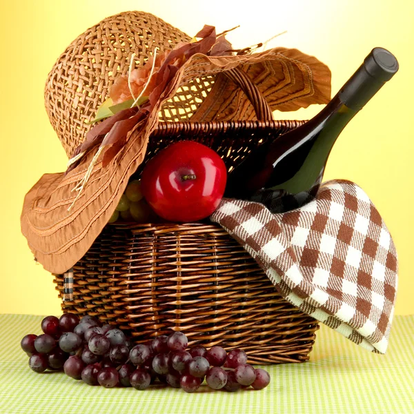 Picnic basket and bottle of wine on cloth on yellow background