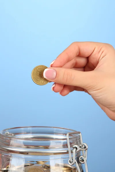Экономия, женская рука положить монету в стеклянную бутылку, на цветном фоне — стоковое фото