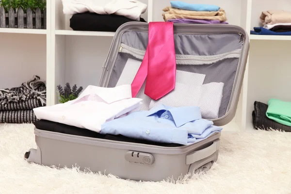 Open grey suitcase with clothing in room — Stock Photo, Image