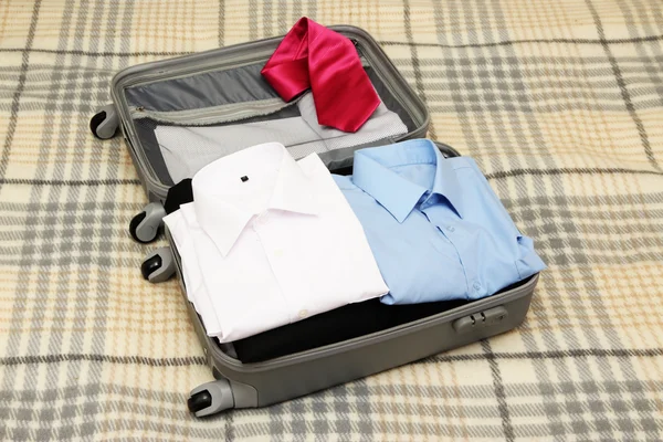 Open grey suitcase with clothing on plaid — Stock Photo, Image