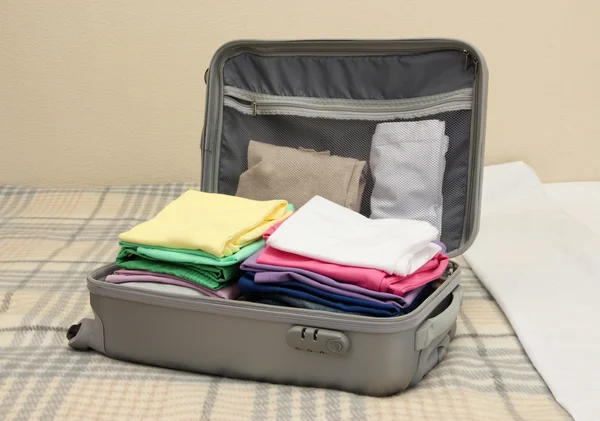 Öppna grå resväska med kläder på sängen — Stockfoto