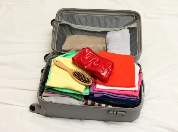 Öppna grå resväska med kläder på sängen — Stockfoto