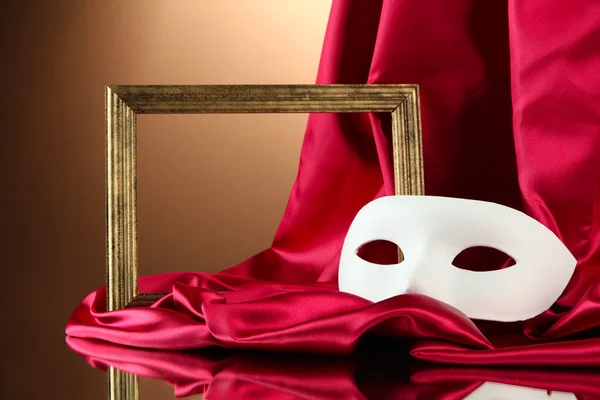 White mask, empty frame and golden silk fabric, on red background — Stock Photo, Image