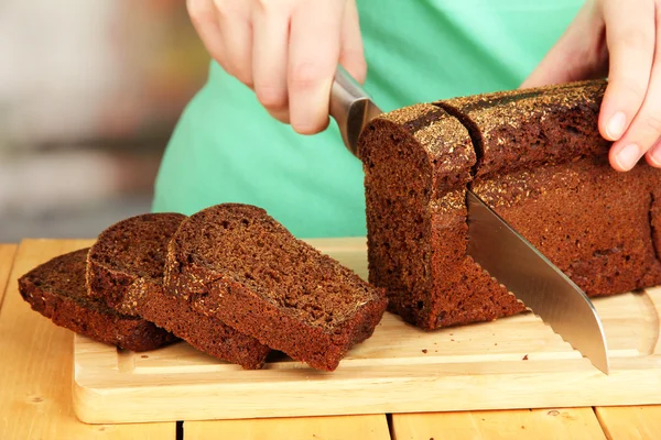 Woman slicing black bread on chopping board on wooden table close up — Stock Photo, Image