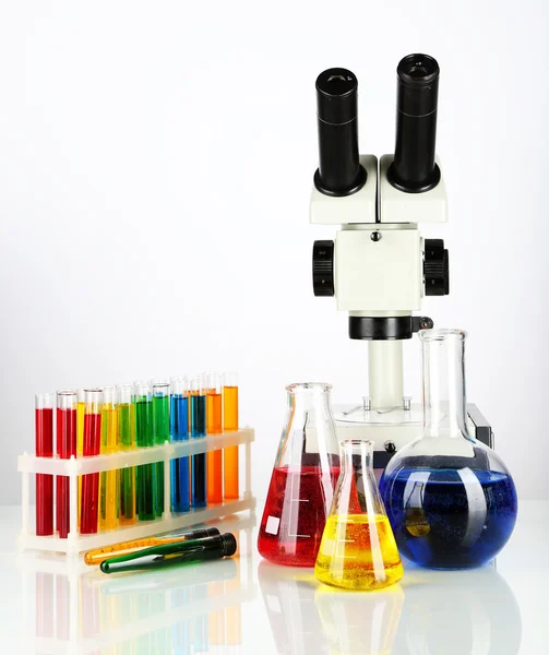 Test tüpleri ile renkli sıvılar ve üzerinde beyaz izole mikroskobu — Stok fotoğraf