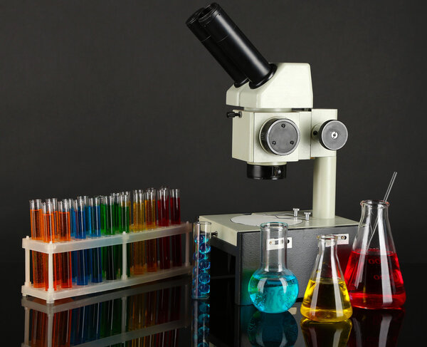 Test tubes with colorful liquids and microscope on dark grey background