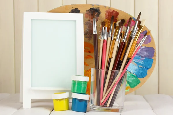 Photo frame as easel with artist's tools on wooden background — Stock Photo, Image