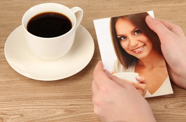 Foto em mãos e xícara de café na mesa de madeira — Fotografia de Stock