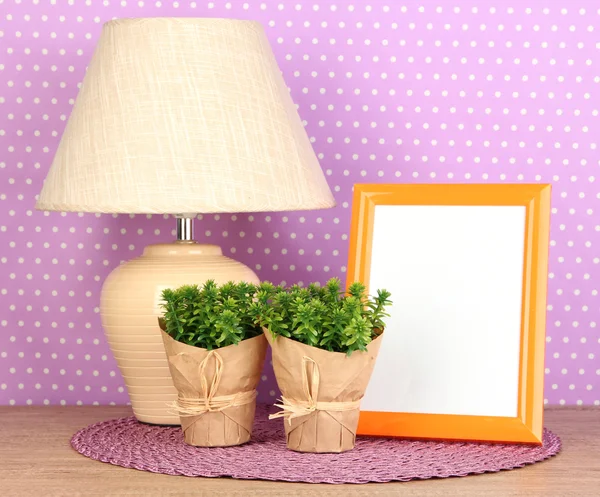 Marco de fotos colorido, lámpara y flores en la mesa de madera sobre fondo de lunares lila — Foto de Stock