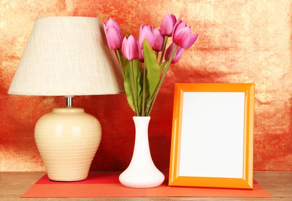 Marco de fotos colorido, lámpara y flores en la mesa de madera sobre fondo rojo — Foto de Stock