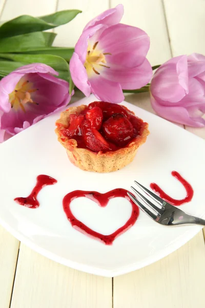Süße Torte mit Erdbeere und Soße auf Teller, auf Holzgrund — Stockfoto