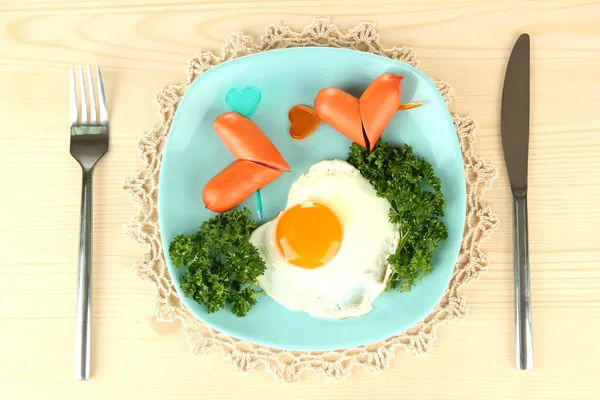 Сосиски у вигляді сердець, яєць і петрушки, на кольоровій тарілці, на дерев'яному фоні — стокове фото