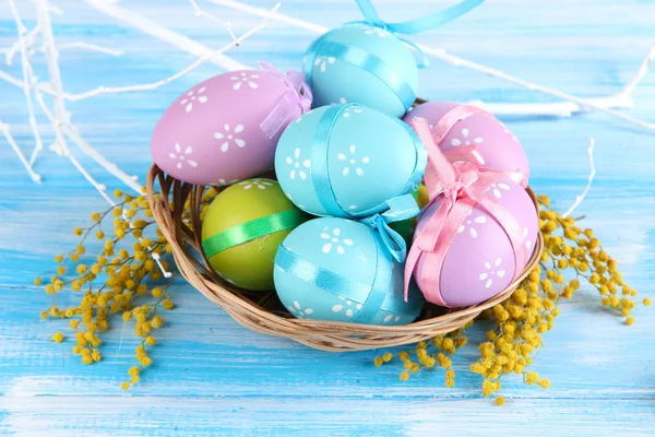 Easter eggs in basket and mimosa flowers, on blue wooden background — Stock Photo, Image