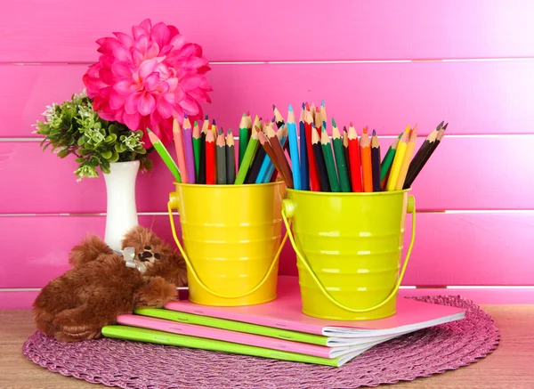 Lápis coloridos em pails com copybooks e urso na mesa sobre fundo rosa — Fotografia de Stock