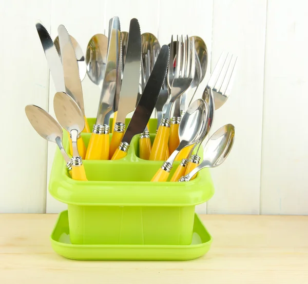 Coltelli, cucchiai, forchette in contenitore di plastica per l'essiccazione, su sfondo di legno a colori — Foto Stock