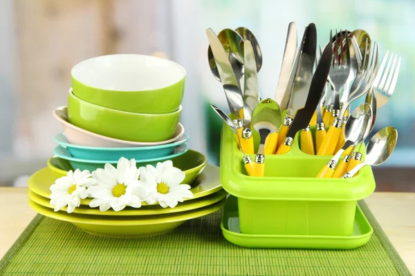 Πιάτα, πιρούνια, μαχαίρια, κουτάλια και άλλα σκεύη κουζίνας σε χαλί μπαμπού, σε φωτεινό φόντο — Φωτογραφία Αρχείου