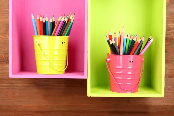 Lápis coloridos em pails em prateleiras sobre fundo de madeira Imagem De Stock