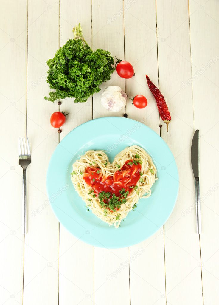 Cooked spaghetti carefully arranged in heart shape and topped with tomato sauce, on wooden background