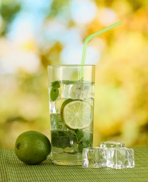 Bicchiere d'acqua con ghiaccio, menta e calce sul tavolo su sfondo luminoso — Foto Stock