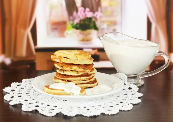 Sweet pancakes on plate with sour cream on table in room — Stock Photo, Image