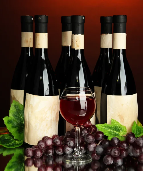 Composition of wine bottles, glass and grape, on dark red background — Stock Photo, Image