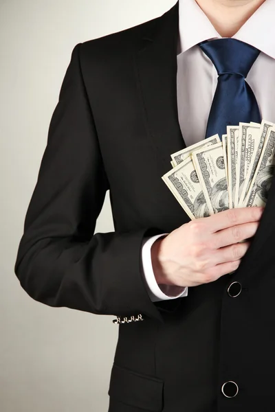 Business man hiding money in pocket on grey background — Stock Photo, Image