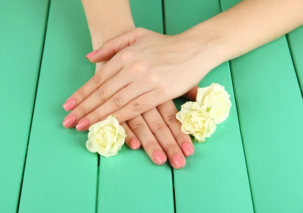 Mains de femme avec manucure rose et fleurs, sur fond de bois couleur — Photo