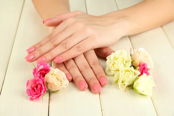 ピンクのマニキュアと木製の背景上の花を持つ女性手 — ストック写真
