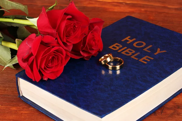 Anéis de casamento na Bíblia com rosas no fundo de madeira — Fotografia de Stock