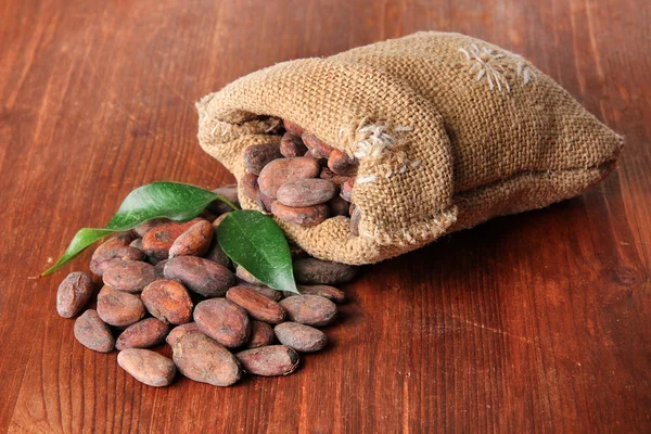 Cacao en bolsa con hojas sobre fondo de madera — Foto de Stock
