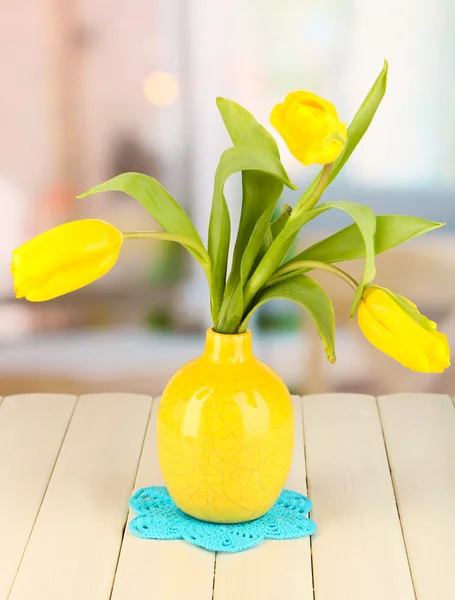 Yellow tulips in vase on wooden table on room background — Stock Photo, Image