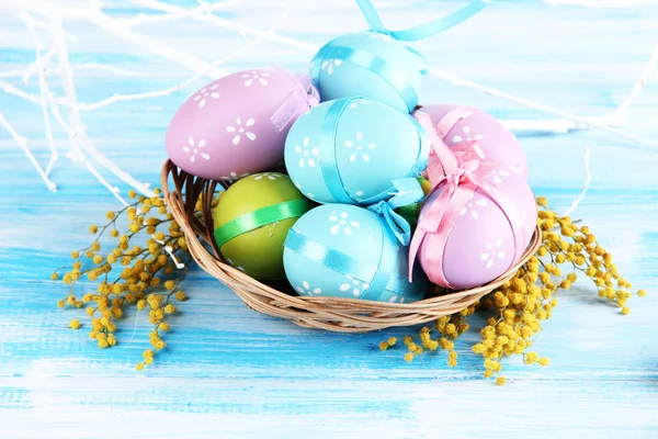 Пасхальные яйца в корзине и цветы мимозы, на синем деревянном фоне — стоковое фото