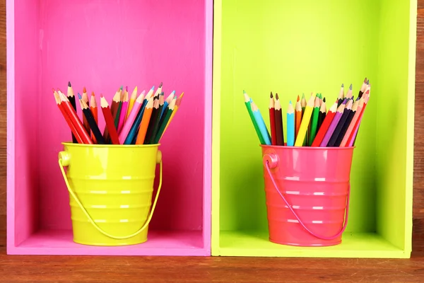 Kleurrijke potloden in emmers op planken op houten achtergrond — Stockfoto