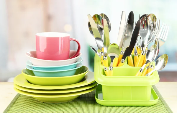 Plates, forks, knives, spoons and other kitchen utensil on bamboo mat, on bright background — Stock Photo, Image