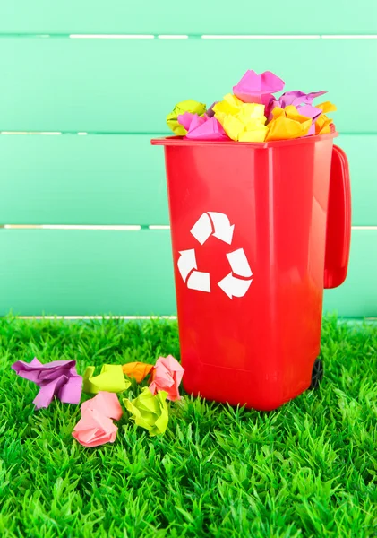 Recycling bin with papers on grass on light blue background — Stock Photo, Image