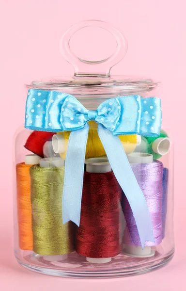 Glass jar containing various colored thread on pink background — Stock Photo, Image